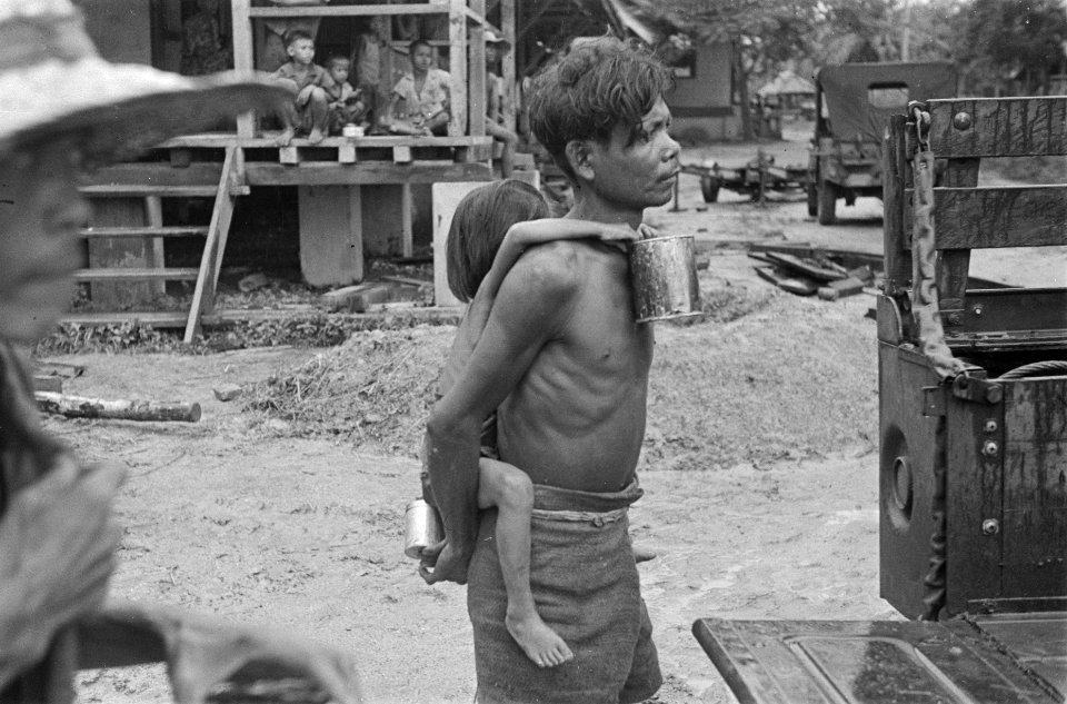 Indonesische man met kind op de rug. Kind houdt een blik vast. Jeeps zijn te zie, Bestanddeelnr 124-2-3