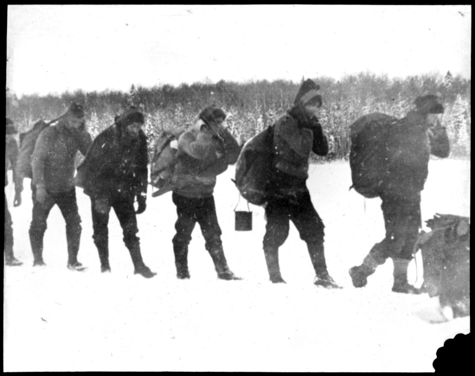 File of men carrying packs on their backs as they walk thr…
