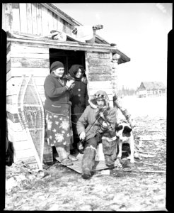 Man playing fiddle for his family outside a hut, Moosonee