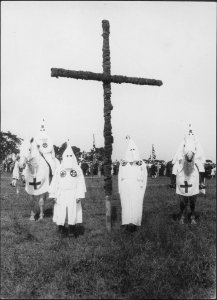 Knights of the Ku Klux Klan standing in front of a cross…