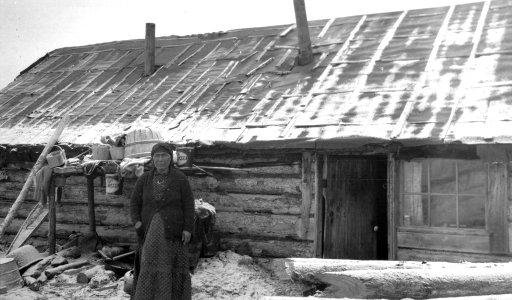 [Indigenous woman at the door of her log cabin]