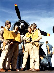 Four pilots converse on flight deck of carrier upon return…