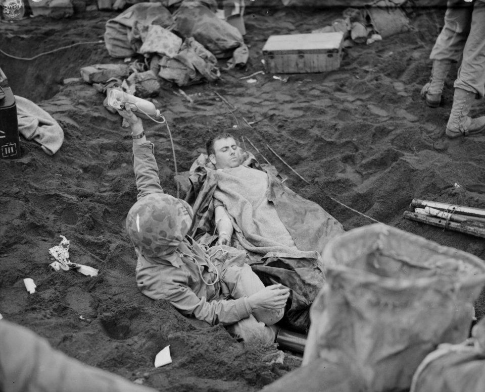 Holding the bottle overhead, a Navy corpsman administers b…