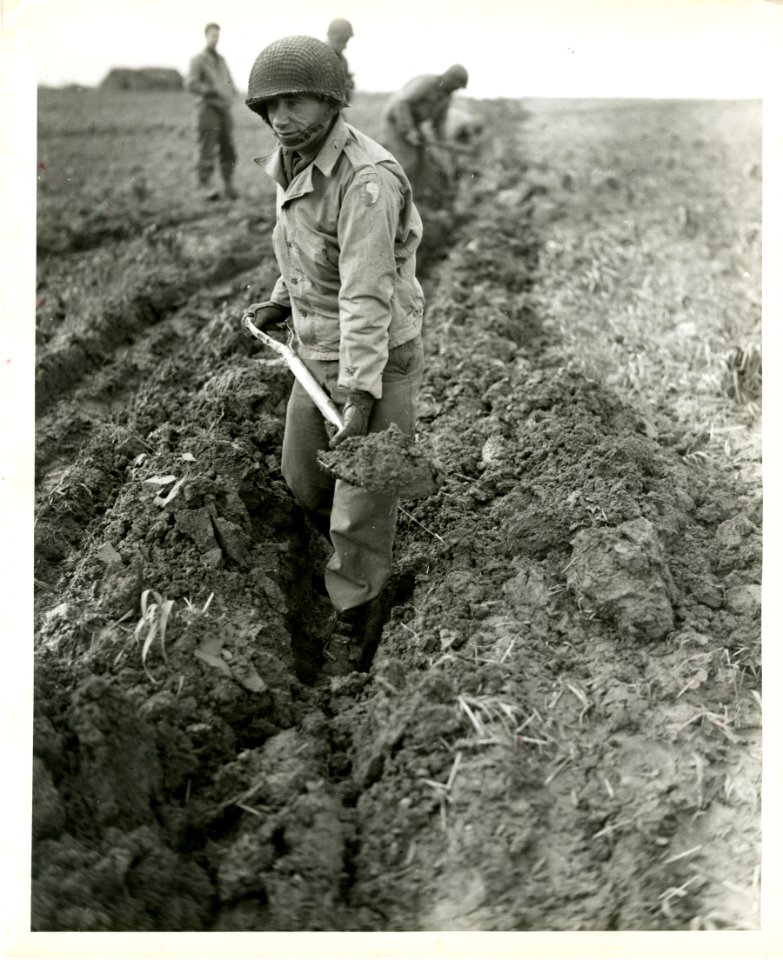 A soldier of the 29th Infantry Division digs out a furrow …