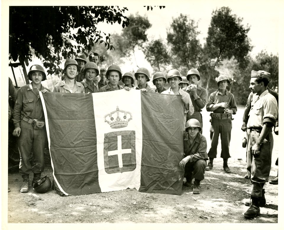 U.S. soldiers pose with a surrendered Italian flag for a C…