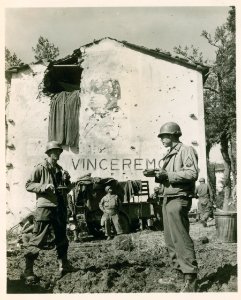 Two US servicemen eat from mess kits in front of bomb dama…