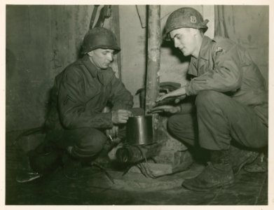 Two GIs of the 1st Armored Division using a stove made out…