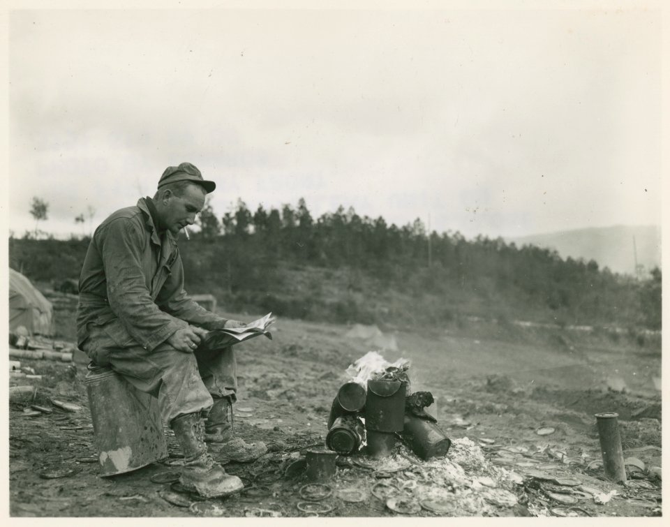 An American soldier reading Yank magazine by a fire in Ita…