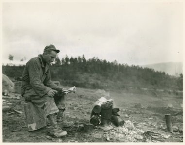 An American soldier reading Yank magazine by a fire in Ita…