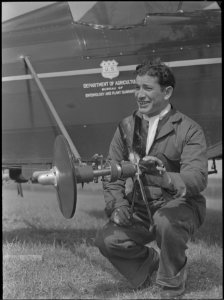 Department of Agriculture worker with insecticide spraying device, and plane used for spraying (37085298434)