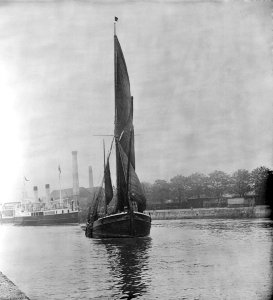 A view across the New Cut at Ipswich with an unidentified spritsail barge under sail leaving. RMG (flipped) P27528