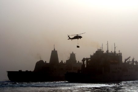 A U.S. Navy MH-60S Seahawk helicopter assigned to Helicopter Sea Combat Squadron (HSC) 26 carries supplies from the dry cargo-ammunition ship USNS Wally Schirra (T-AKE 8), right, during a vertical replenishment 110717-N-RC734-091