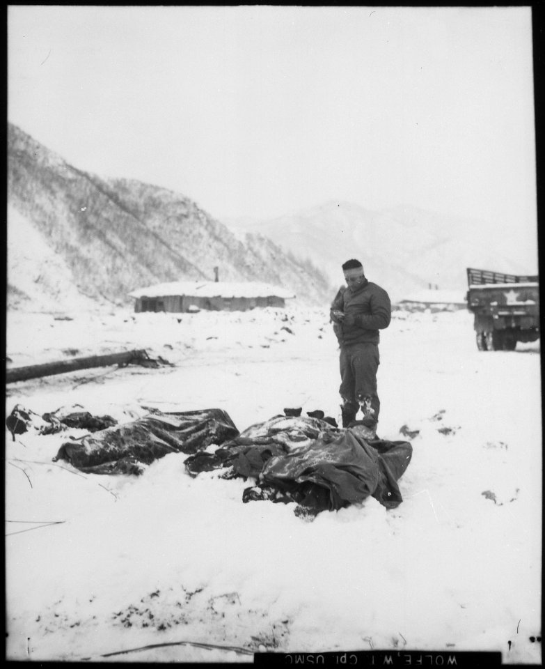 A wounded chaplain reads a memorial service over the snow-covered bodies of dead Marines. Koto-ri, Korea. - NARA - 532413