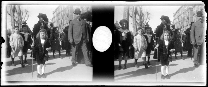 Adults i infants vestits de diumenge passejant per un carrer de Barcelona