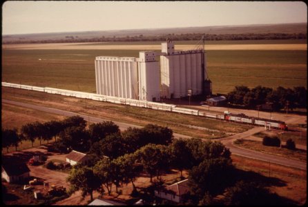 Aerial-view-of-the-southwest-limited-train-3-as-it-passes-a-farm-co-op-elevator-between-dodge-city-and-garden-city-kansas-june-1974 7158229710 o