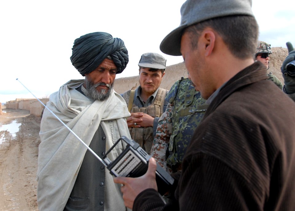Afghan Police officer hands out radios keyed to RADIO GURESHK in Mayai Village, Gureshk district, Helmand Province,