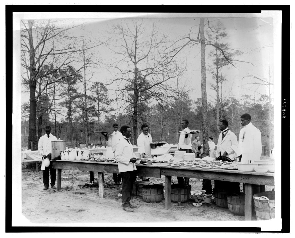 African American men preparing to serve a meal in an outdoor setting among trees LCCN2008677114