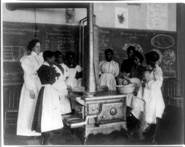 African American schoolgirls with teacher, learning to cook on a wood stove in classroom LCCN2001699122