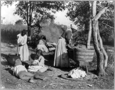 African-American woman doing laundry with a scrub board and tub, African-American girl stirring pot with 3 other children on the ground watching, and a woman in the background spreading LCCN2006679024