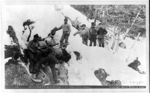 Alaska - Klondike - Devil's Bluff portage in the canyon near Sheep Camp; group of 8 African Americans and Whites making portage LCCN2006690157