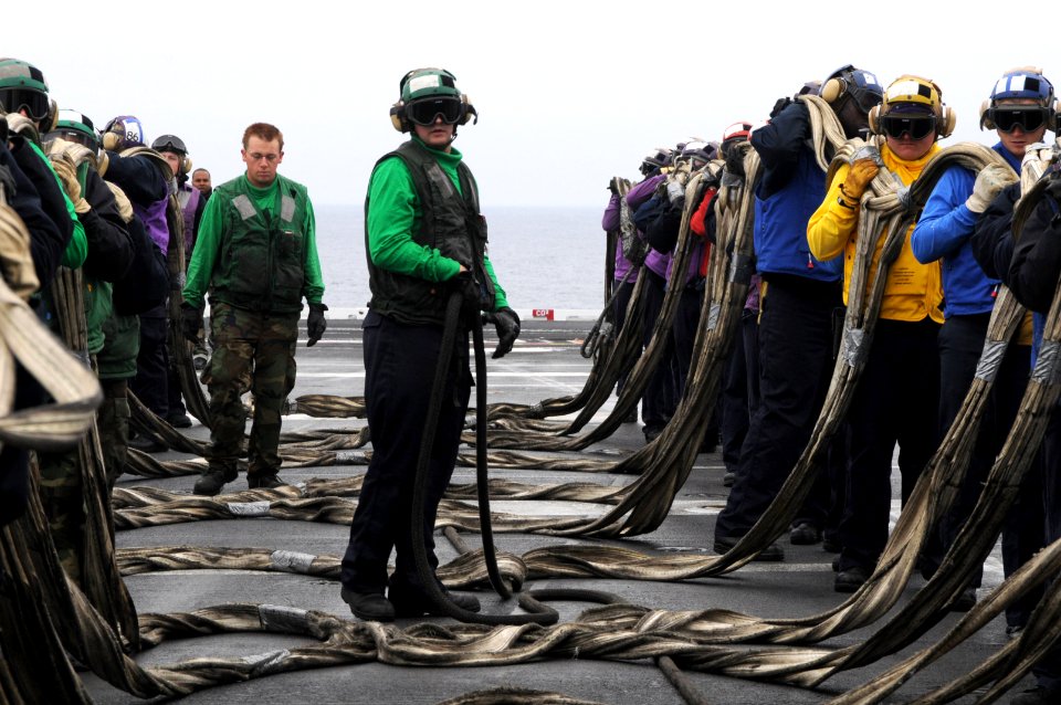Aviation Boatswain's Mate (Equipment) Airman Alexander Miller, center, prepares to stow a barricade below the flight deck of the aircraft carrier USS Ronald Reagan (CVN 76)