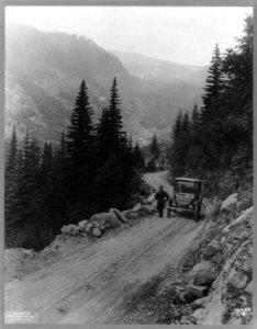 Detroit Electric auto on promotional tour through mountains from Seattle to Mt. Rainier- Man standing in front of auto, which is parked on mountain road LCCN2003653830