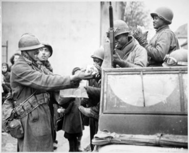 Two smiling French soldiers fill the hands of American soldiers with candy, in Rouffach, France, after the closing of t - NARA - 531247