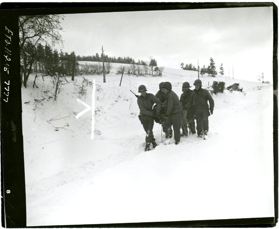 111-SC-199231 - A wounded soldier is carried back to the aid post by his comrades, on a stretcher improvised from a door on which straw has been placed