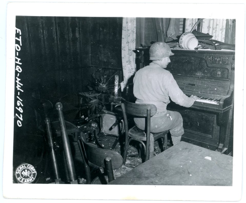 111-SC-195022 - PFC R. Larock, Helena, Mont., relaxes after battle by playing piano in a wrecked German beer hall