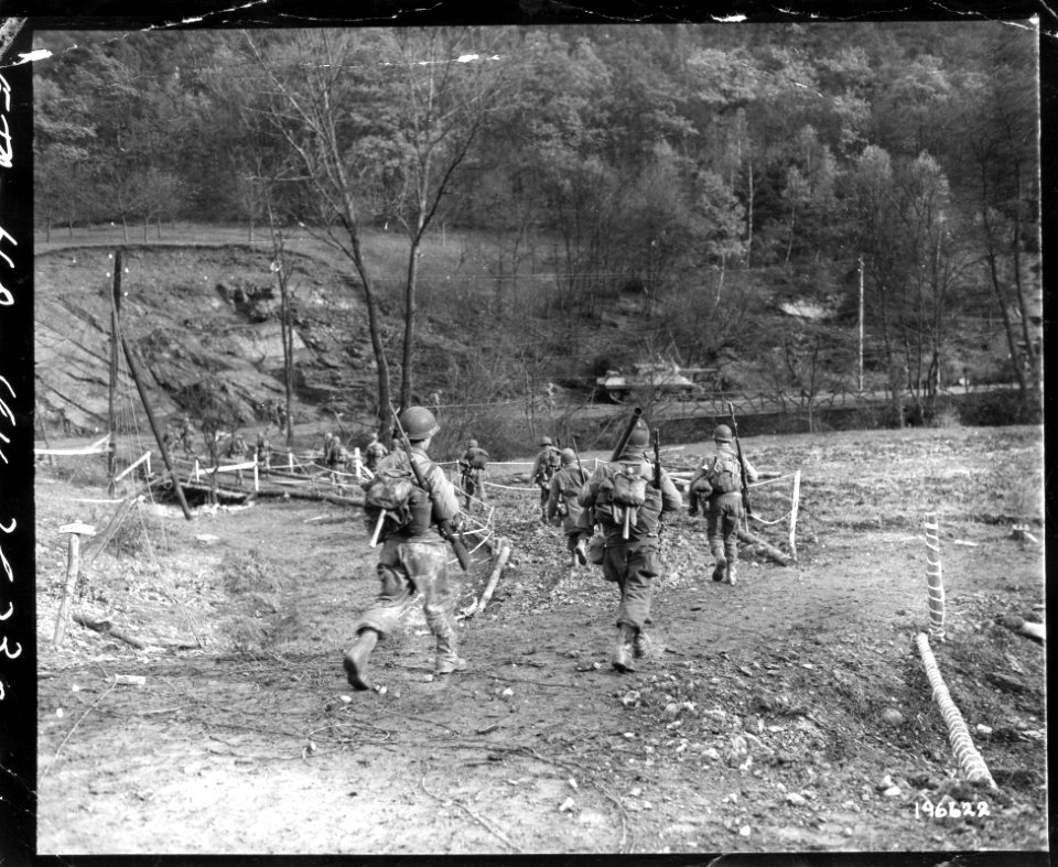111-SC-196622 - Deep in the Hurtgen forest, in Germany, American infantrymen move across a bridge over a small stream. A tank, part of the new Allied offensive, can be seen in the background