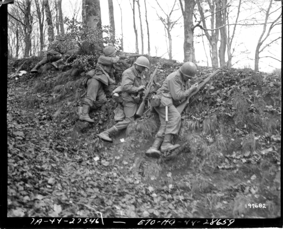 111-SC-197682 - SC 197682 - An American infantryman keeps firing while two of his comrades insert fresh ammunition in their rifles, as steady fire from this sheltered infantry covers advance near Rosteig, France. December 5, 1944