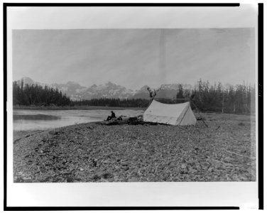 A man, possibly B.E. Fernow, seated next to river, tent on the right, mountains in background, Alaska, 1899) - Curtis LCCN2002706852