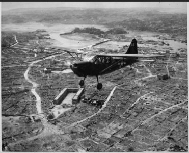 A Marine observation plane flies low over Naha, capital of Okinawa. On this flight, the tiny ship drew small arms and... - NARA - 532379 photo