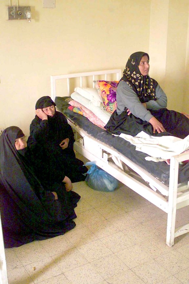 A patient at the Karbala City Women Hospital, in Karbala, Iraq, sits up on an outdated hospital bed while family members sit on the floor. DM-SD-04-04692
