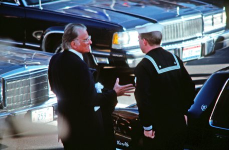 A sailor assists Reverend Billy Graham from his car