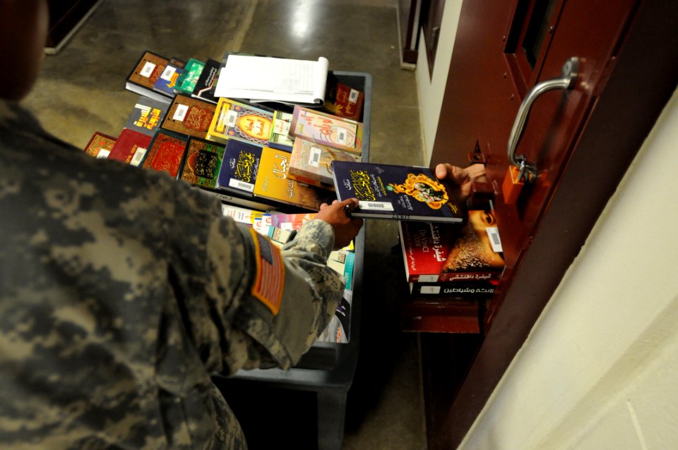 A soldier from the detainee library hands a book to a detainee in Camp Five DVIDS368266