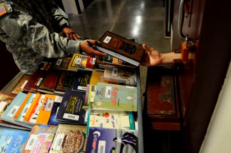 A soldier from the detainee library hands a book to a detainee in Camp Five DVIDS368275