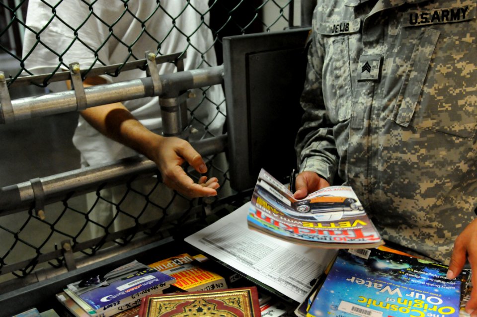 A soldier from the detainee library hands a periodical to a detainee in Camp Five DVIDS368267