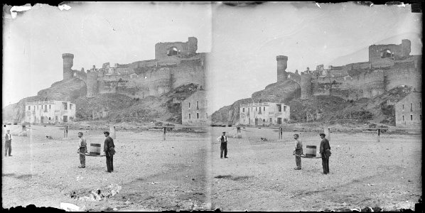 Alguns homes a la platja i al fons la vila vella , muralles i torres a Tossa de Mar