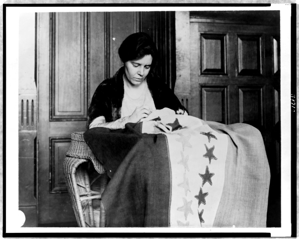 Alice Paul, half-length portrait, seated, facing slightly right, sewing suffrage flag LCCN97519946