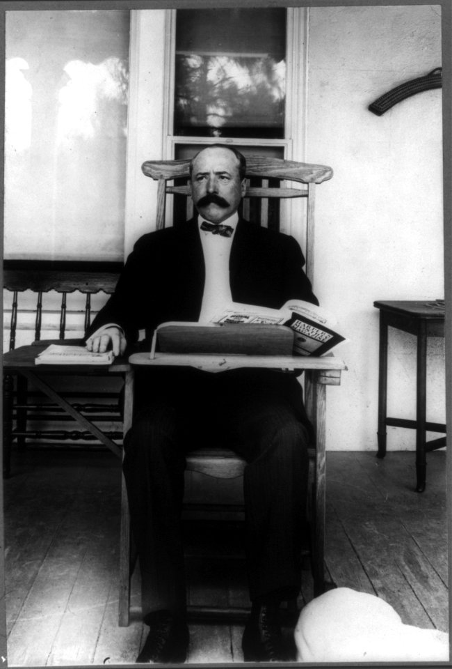 Alton Brooks Parker, 1852-1926, full length portrait, seated, facing slightly left; in classroom desk chair reading Harper's Magazine LCCN2005686641