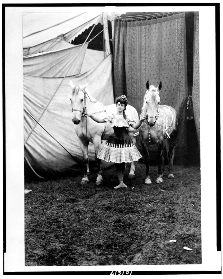 Bareback rider standing between two horses outside circus tent LCCN90712947