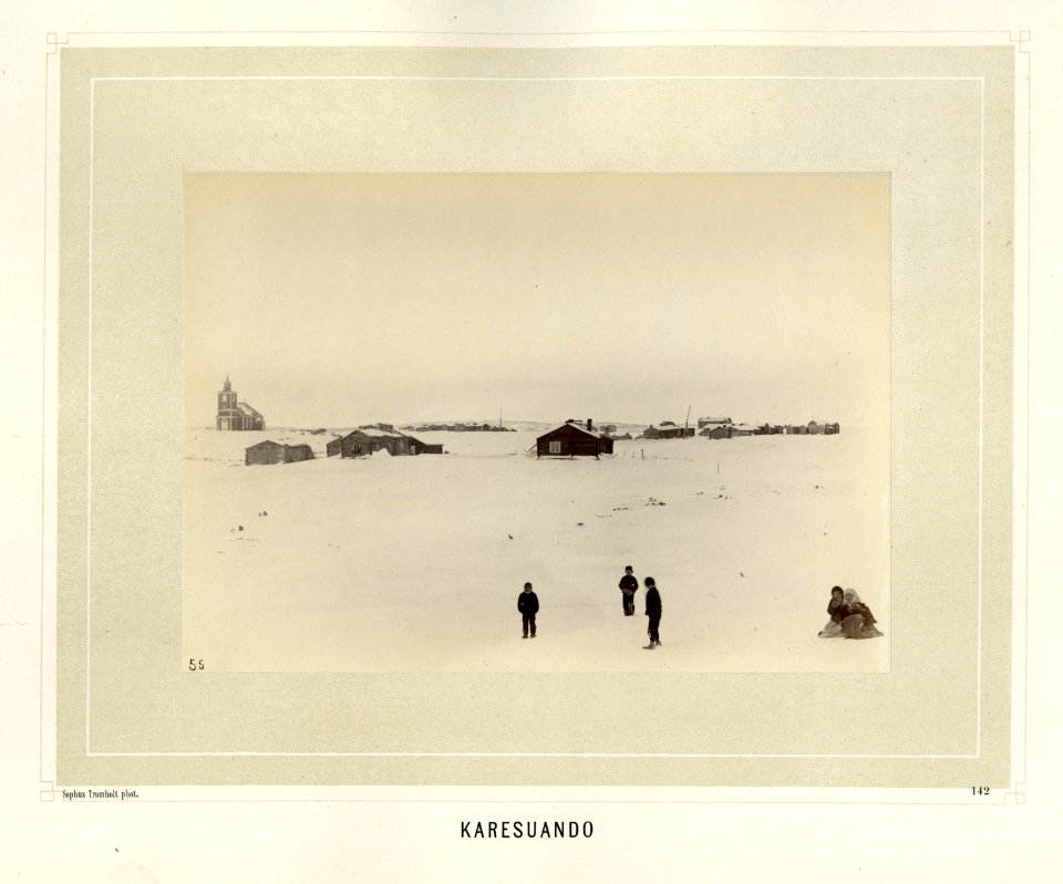 Barn leker i snøen foran bebyggelse med kirke i Karesuando i Kiruna i Norrbotten i Sverige - Norsk folkemuseum - NF.15006-136