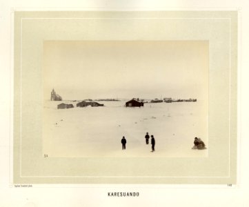 Barn leker i snøen foran bebyggelse med kirke i Karesuando i Kiruna i Norrbotten i Sverige - Norsk folkemuseum - NF.15006-136