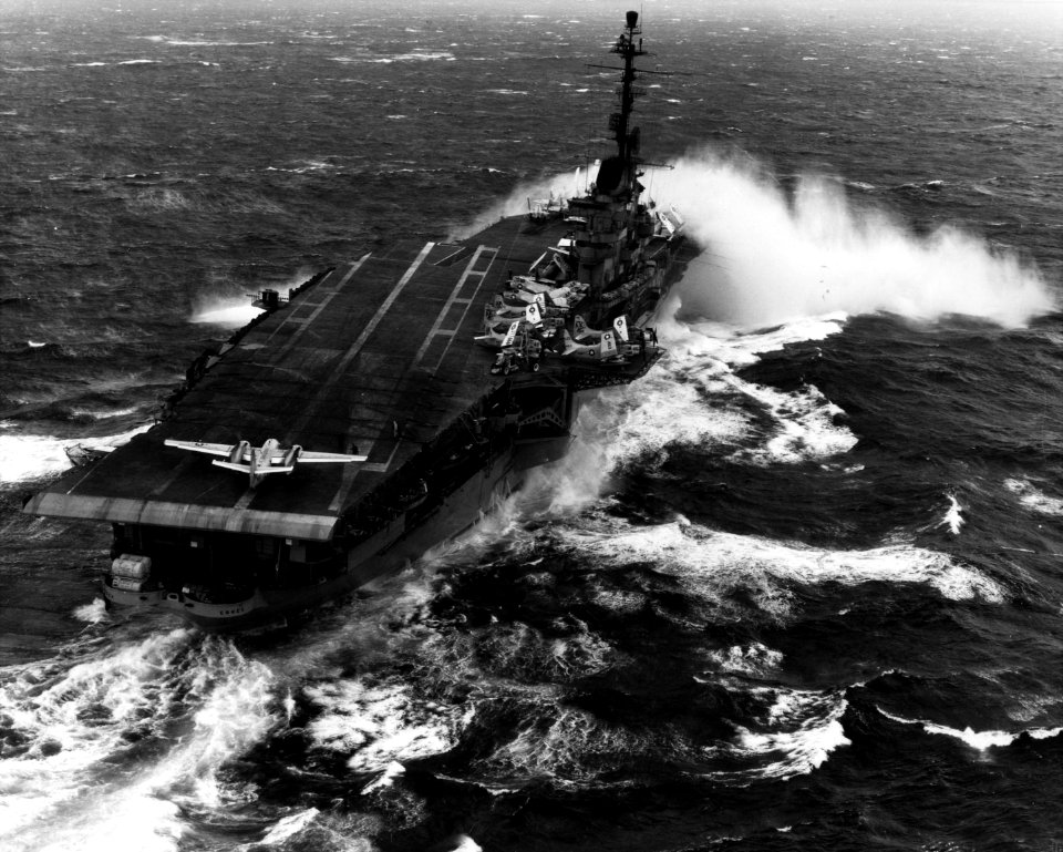USS Essex (CV-9) Takes spray over the bow while steaming in heavy seas, Note S2-F at the rear of the flight deck, with its engines turning. Other planes visible, amidships, include AD and F4-D January 12th 1960 . (51002958560)