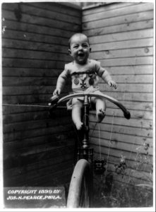 Baby with sports medals perched on bicycle held upright by rope LCCN92521065