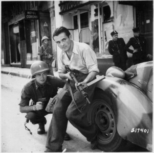 American officer and French partisan crouch behind an auto during a street fight in a French city. - NARA - 531322 photo