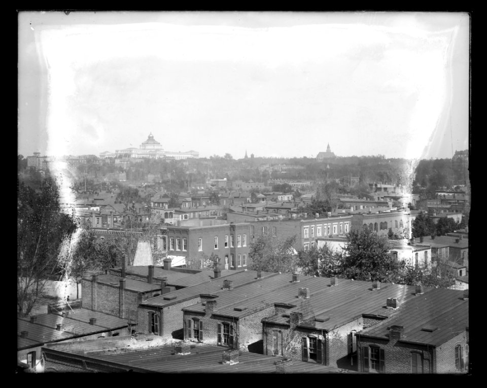 An elevated view of roof tops of row houses and other buildings, showing the Library of Congress, Jefferson building in the distance LCCN2016647110