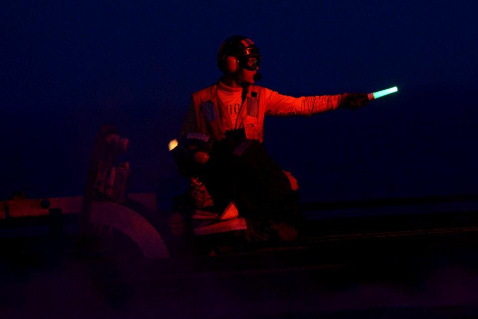 An officer signals an aircraft for launch at night. (8428932987)