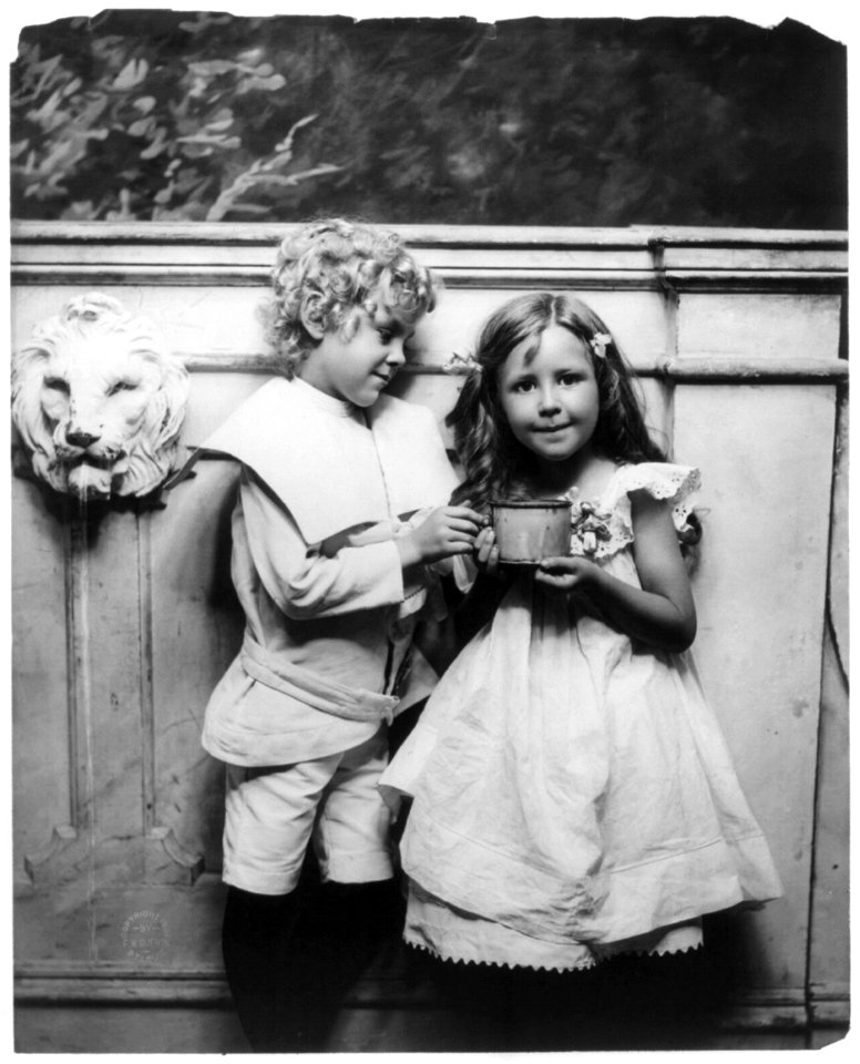 Boy and girl posed, three-quarter length, standing, holding large cup LCCN96505512
